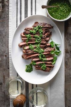 a white plate topped with meat covered in pesto next to two glasses of water