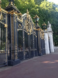 an iron gate with gold and black decorations on the top, along side a sidewalk