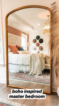 a large mirror reflecting a bed in a room with wood floors and white walls on the wall