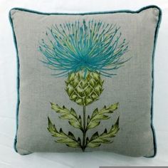 a blue and green flower on a white pillow sitting on top of a gray couch