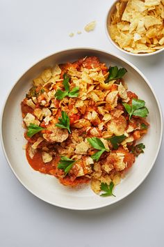 a white plate topped with lots of food next to a bowl filled with potato chips