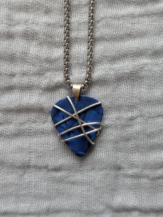 a blue heart shaped pendant with silver lines on the front and back of it hanging from a chain