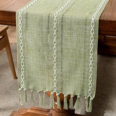 a green table runner with tassels on top of it in front of a wooden table