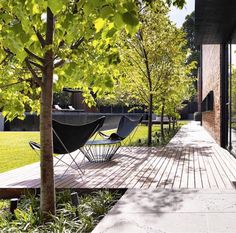 two black chairs sitting on top of a wooden deck next to a green field and trees