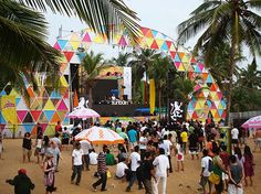 a large group of people standing around in front of a stage with colorful umbrellas