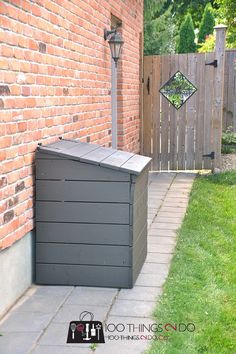 an outdoor trash can sitting next to a brick wall and green grass in front of it