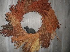 a cat sitting on top of a wreath made out of dry grass and dried plants