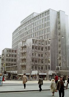 people walking on the sidewalk in front of a large building with many windows and balconies