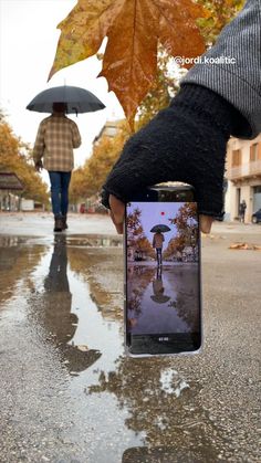 a person holding an open cell phone in their hand while walking down the street with an umbrella