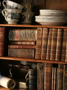 an old bookshelf filled with lots of antique books and bowls on top of them