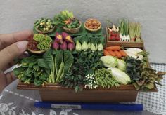 a person holding a tray full of fresh vegetables on a table with other fruits and veggies