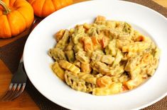 a white bowl filled with pasta next to two pumpkins and a fork on a wooden table