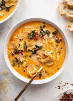 two bowls of soup with bread on the side and one bowl is filled with tortellini shells