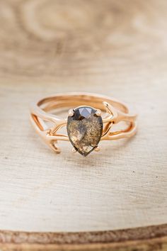 a gold ring with a heart shaped stone on it's side, sitting on top of a wooden surface