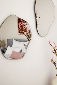 two mirrors on the wall above a vase with flowers