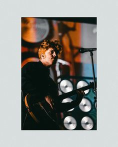 a man with red hair playing guitar in front of a microphone and some lights behind him