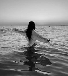 a woman standing in the water with her arms spread out and looking at the sky