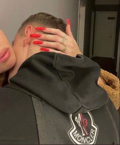 a woman with red nail polish covering her face next to a man in a black jacket