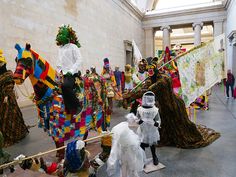 several people dressed up in costumes and holding flags at an art gallery with other people standing around