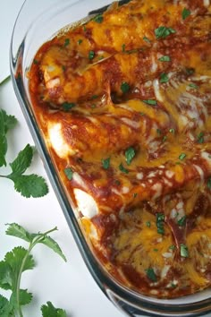 a casserole dish with cheese, sauce and herbs on the side for garnish