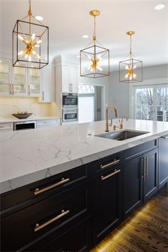 a kitchen with marble counter tops and gold accents on the lights hanging from the ceiling