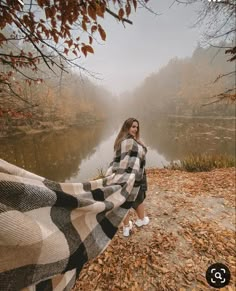 a woman wrapped up in a blanket by the water on a foggy autumn day