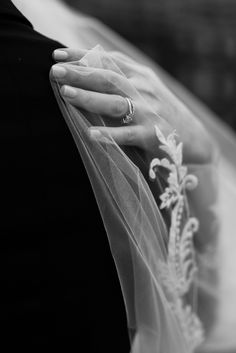 black and white photograph of the bride's wedding ring on her finger as she stands with her veil draped over her shoulder