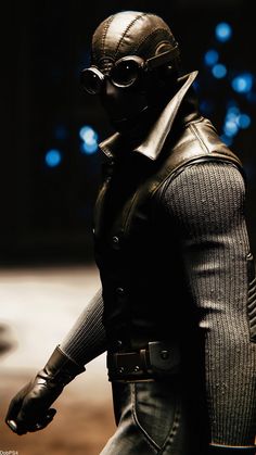 a close up of a figurine wearing a leather outfit and goggles with lights in the background