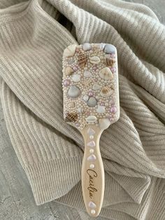 a wooden comb with shells and pearls on it sitting on top of a white sweater