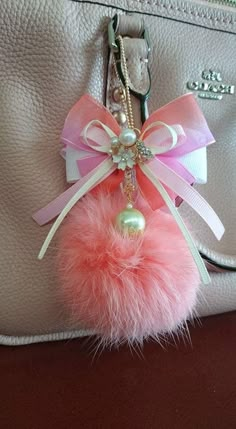 a pink pom - pom keychain hanging from a white purse