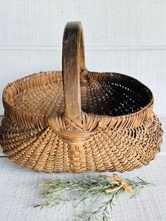 a wicker basket sitting on top of a white cloth covered floor next to a sprig of rosemary