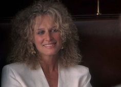 a close up of a person wearing a white shirt and smiling at the camera with curly hair