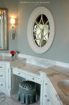 a bathroom with marble counter tops and white cabinets, along with a round mirror above the sink