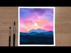 a watercolor painting of mountains with the sun setting in the distance and a pen next to it