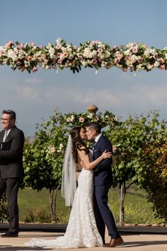 a bride and groom kissing under an arch with flowers