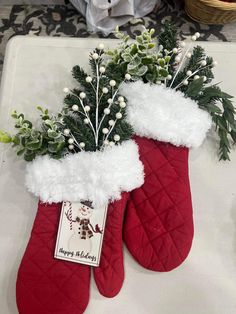 two red christmas stockings with white flowers and greenery in them on a counter top