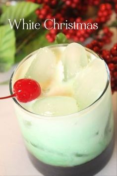 a green drink with ice and a cherry on the top is sitting in front of red berries