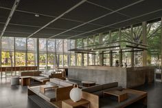 a large open room with couches and tables in front of glass walls that look out onto the trees