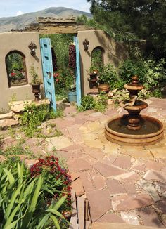 a painting of an outdoor fountain surrounded by greenery and potted plants with blue doors in the background