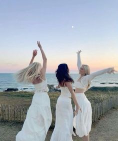 two women in white dresses are dancing near the ocean