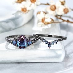 two rings with blue stones on them sitting on a white plate next to flowers and a vase