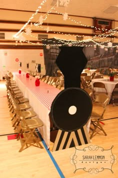 a long table with chairs and a train on it in a room that has lights strung from the ceiling