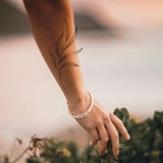 a woman's hand with a feather tattoo on her left arm and wrist, in front of some flowers