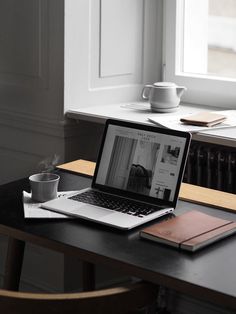 an open laptop computer sitting on top of a wooden desk next to a cup of coffee