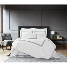 a bed with white sheets and pillows on top of a wooden floor next to a chair