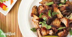 meat with cilantro and parsley on a white plate next to a lime wedge