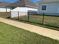 a black fence is in front of a white house and some grass on the sidewalk