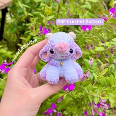 a hand holding a small stuffed animal in front of some purple and pink flowers,