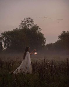 a woman in a white dress is holding a lantern and birds are flying above her