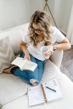 a woman sitting on a couch reading a book and holding a coffee cup with her right hand